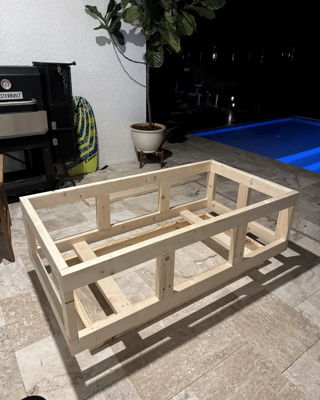 The bare two-by-four frame of the fire table, standing on the patio at night